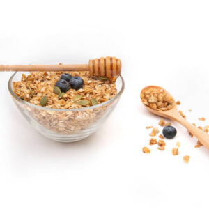 Energy granola on a clear bowl with honey on a white background.