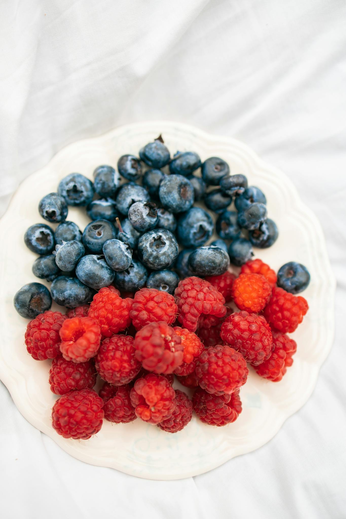 Close-up of fresh blueberries and raspberries on a white plate, showcasing nutritious organic fruits.