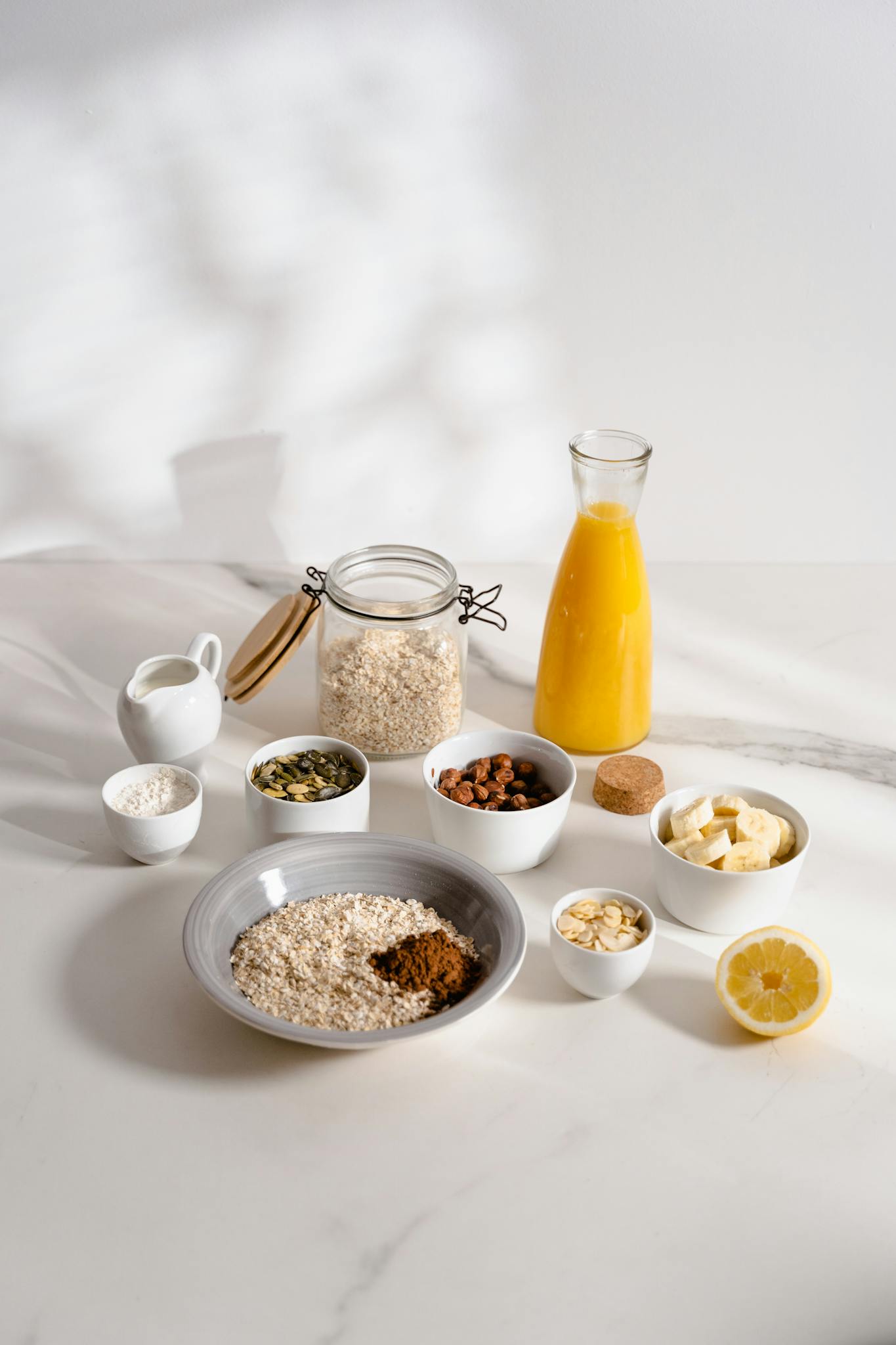 Flat lay of wholesome breakfast ingredients including oatmeal, nuts, banana, pumpkin seeds, and juice on a white surface.