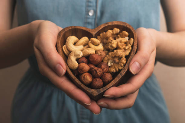 Woman holding heart shaped plate with mixed nuts. close up